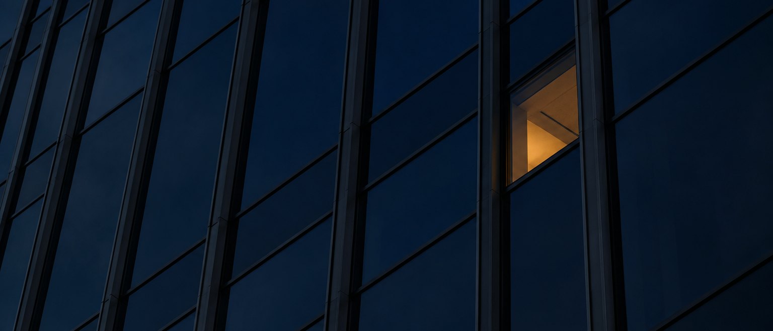 A glass facade at dusk with one lit window